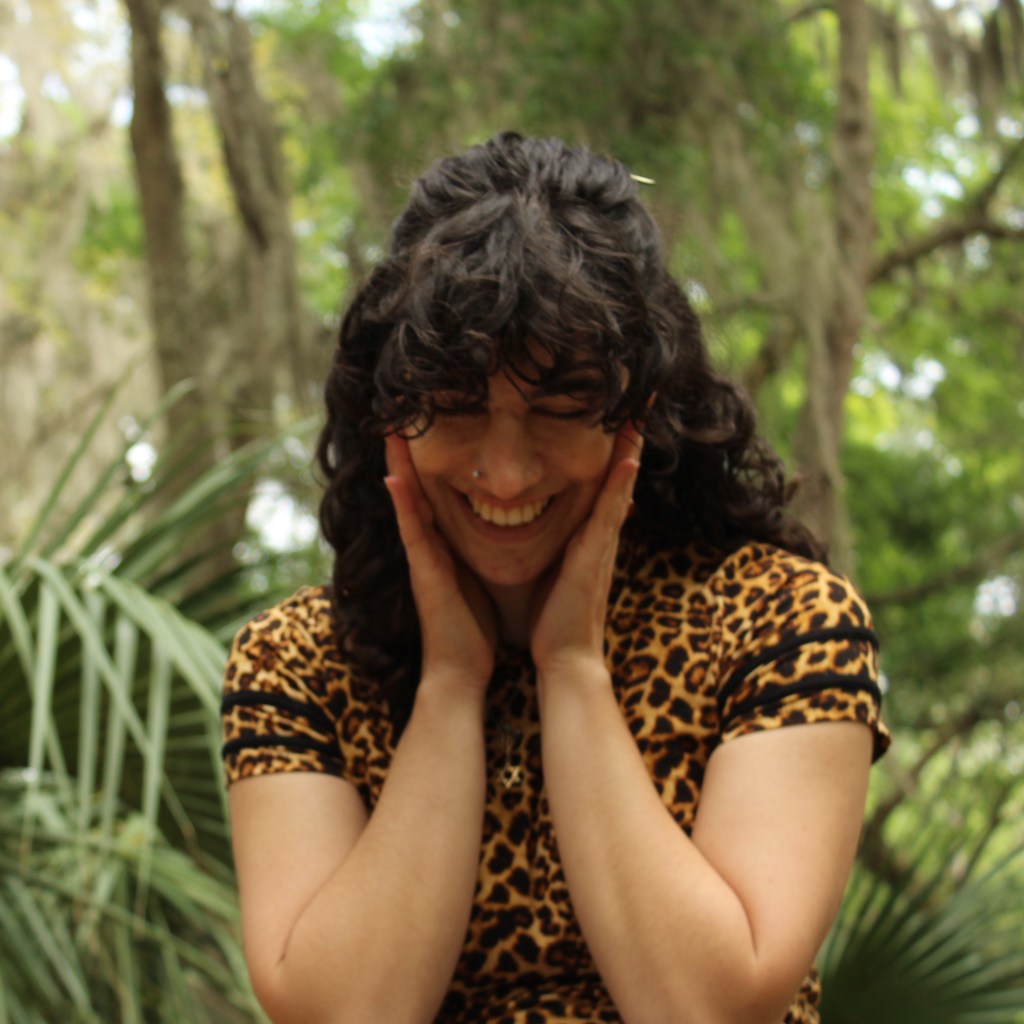 A candid portrait of me at a Florida botanic garden, blushing and holding the sides of my cheeks as I look down.