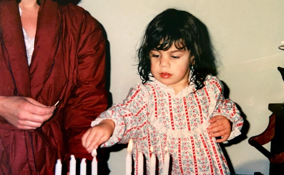 Three-year-old Rebecca very carefully uses a candle to light the other eight candles of her menorah.