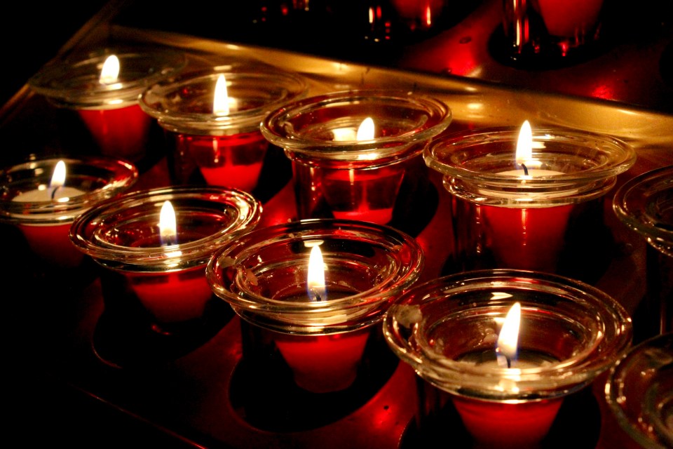 A row of votive candles burn in red glass holders.