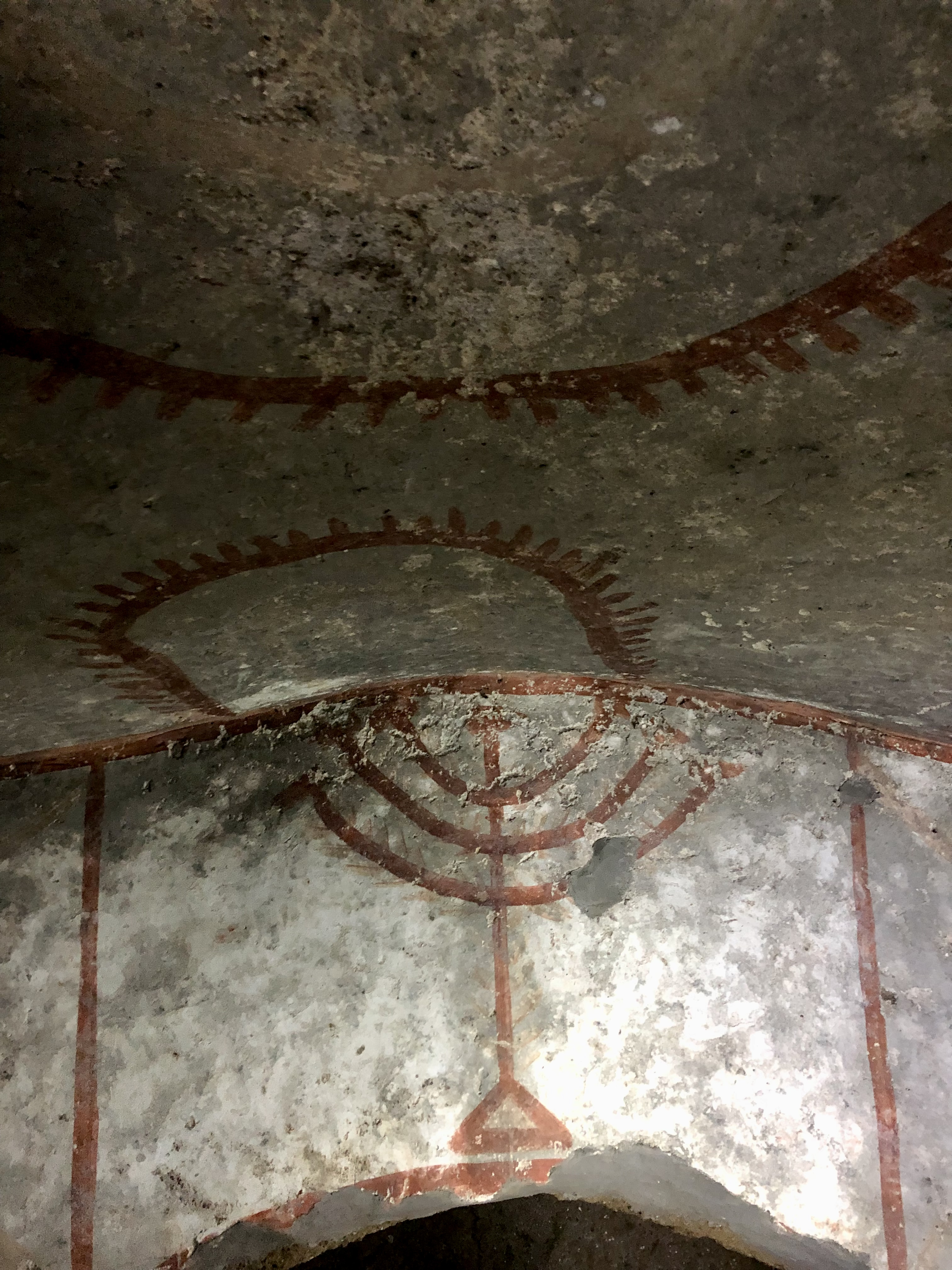 A fresco of a menorah painted above an archway leading to a private burial chamber within the catacombs.