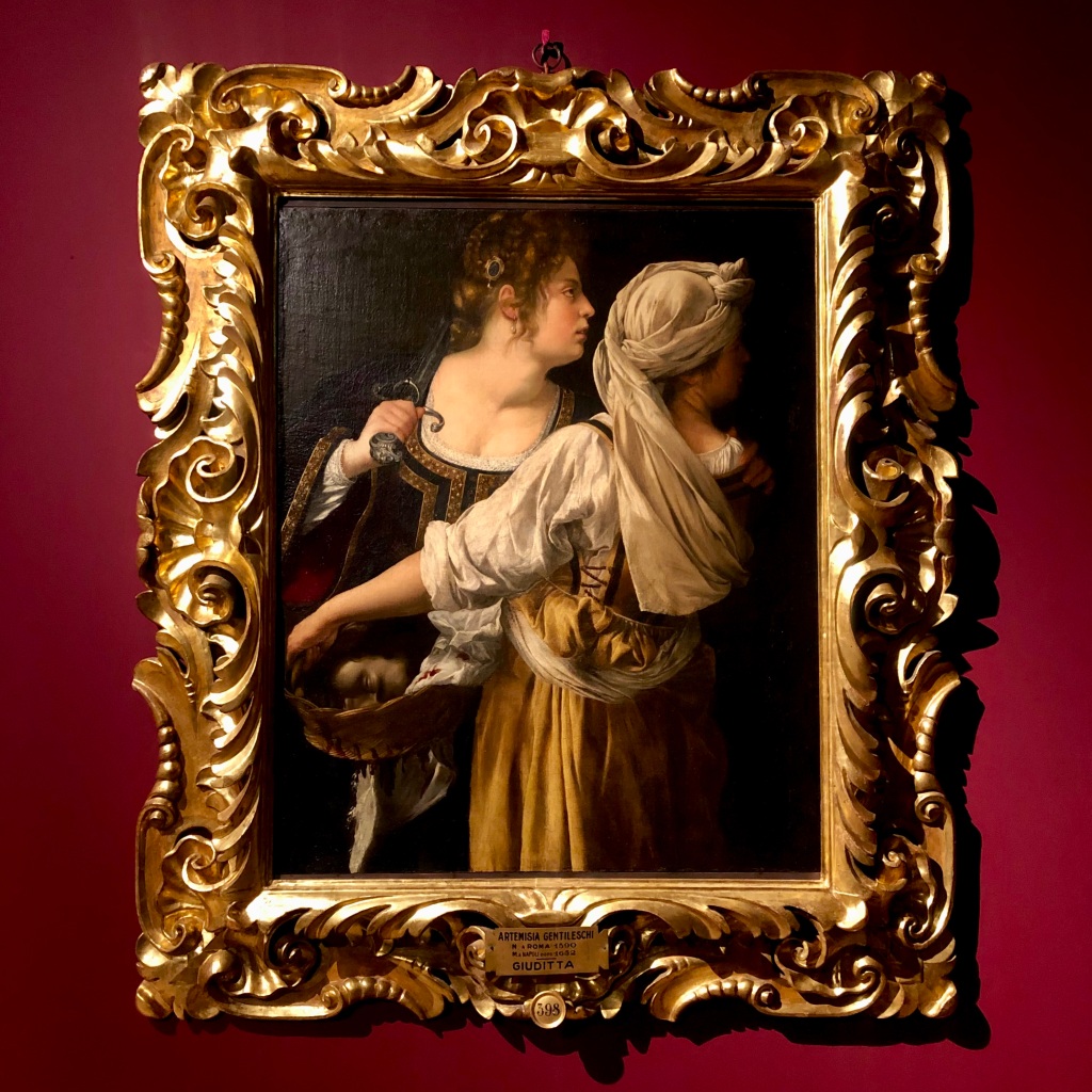 Artemisia Gentileschi's painting of Judith and her handmaid Abra fleeing with the head of Holofernes. Abra holds the head in a basket while Judith carries the sword resting on one shoulder. Her other hand rests gentle on Abra's shoulder.