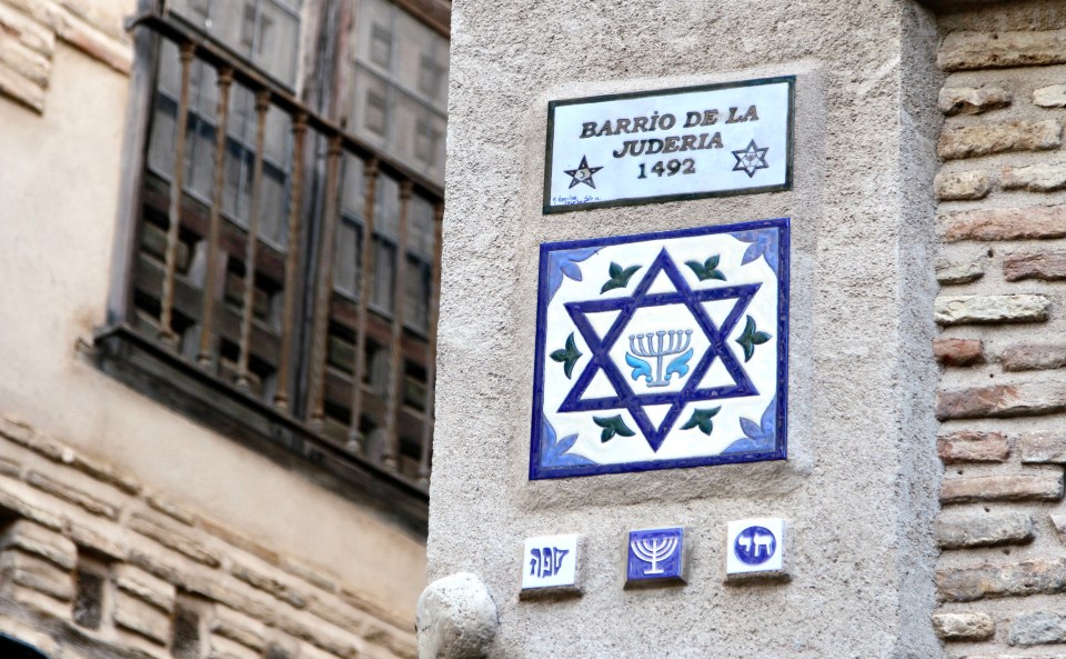 Set into the corner of an old building, a tile reads "Barrio de la Juderia 1492" above another tile with a Star of David and menorah design