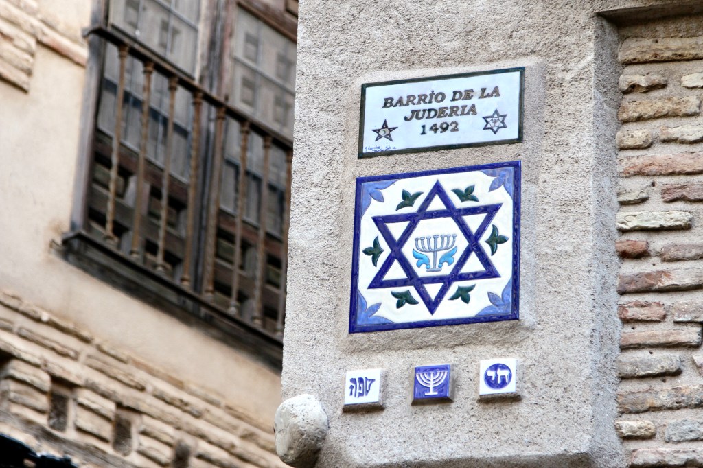 Set into the corner of an old building, a tile reads "Barrio de la Juderia 1492" above another tile with a Star of David and menorah design