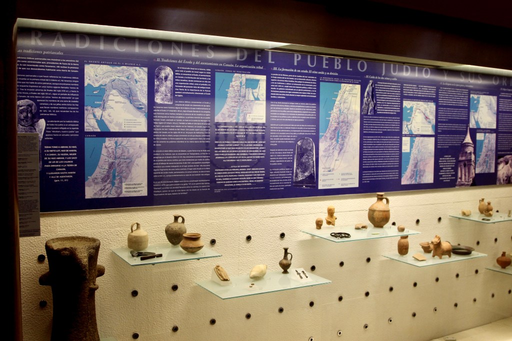 A museum display showcases ancient ceramic pots under a dense wall of text explaining the "Tradiciones del Pueblo Judio" (Traditions of the Jewish People).