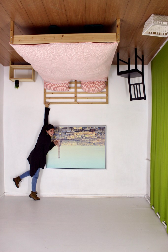 A young woman holds onto the frame of a bed which has been fastened to the ceiling.