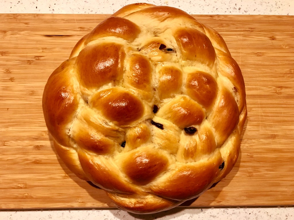 A six-strand round braided challah sits on a wooden cutting board.
